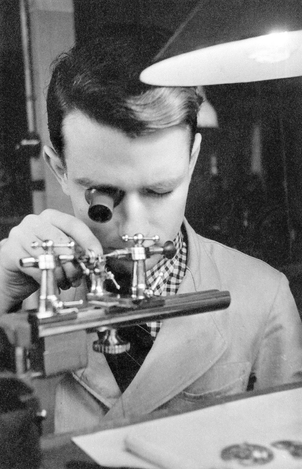 Walter Lange, an elderly man in a suit, examining a wristwatch, with the Glashütte workshop behind him