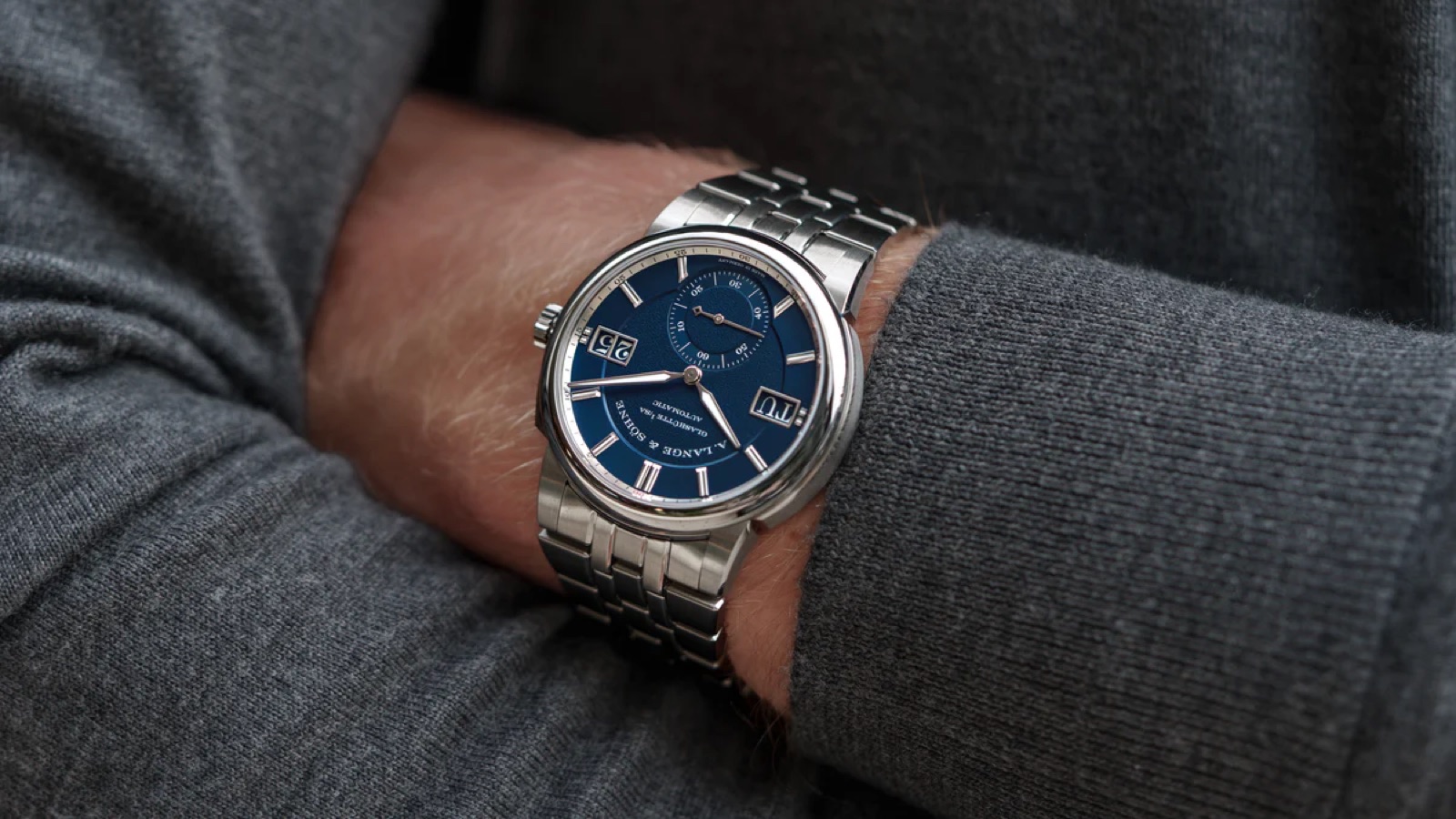 The steel Odysseus on a wrist, showing its integrated bracelet and the day and date windows flanking the dial